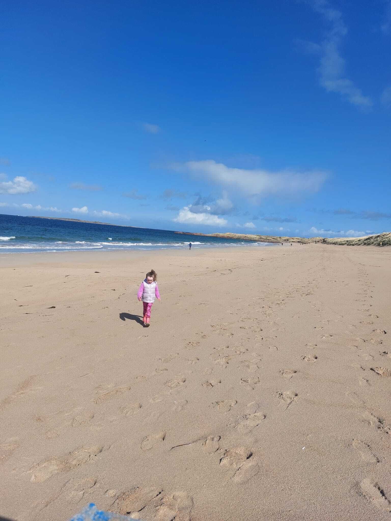 A wide sandy beach with footprints leading towards the ocean.