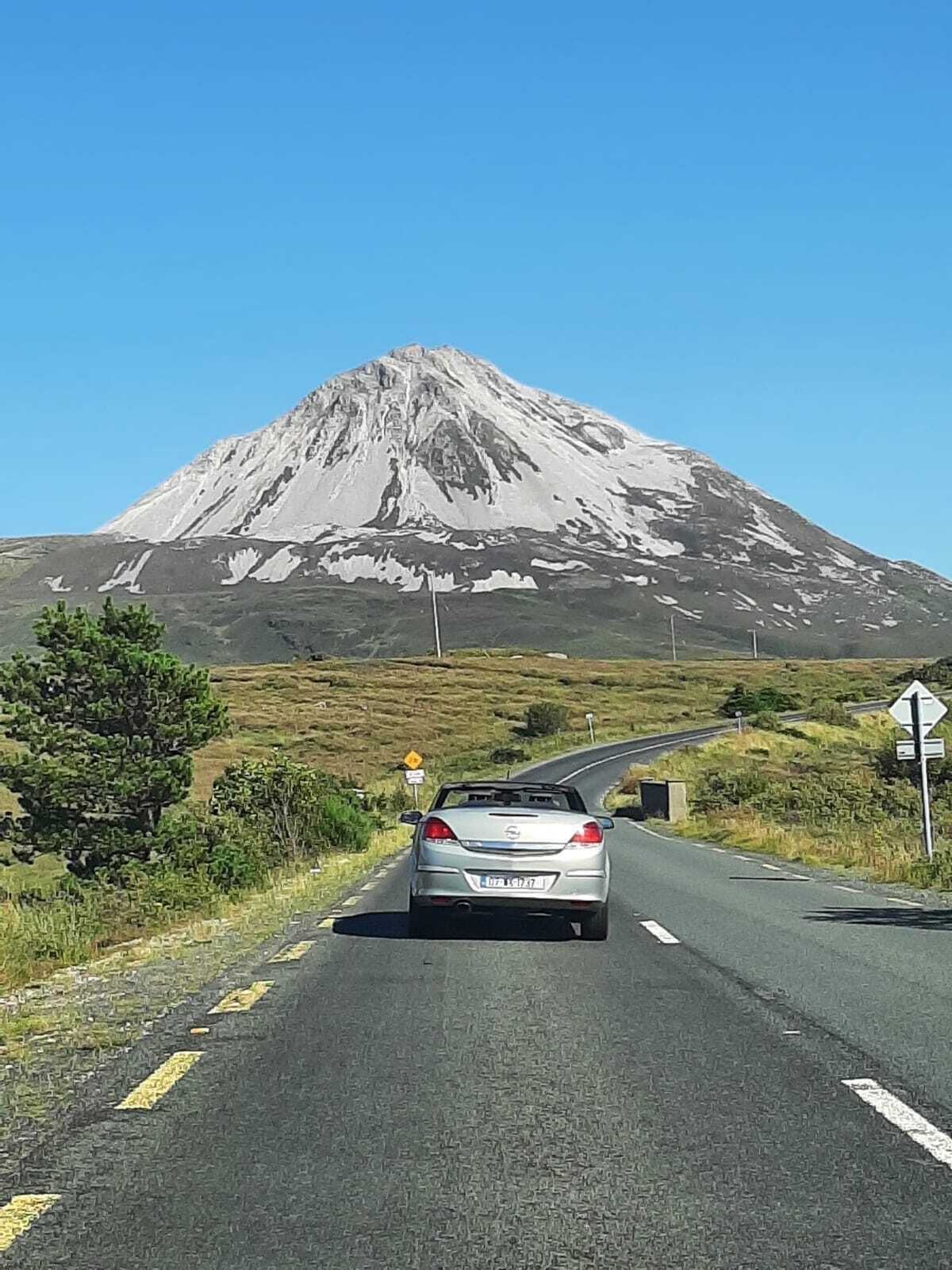 A car driving on a road with a mountain in the background.