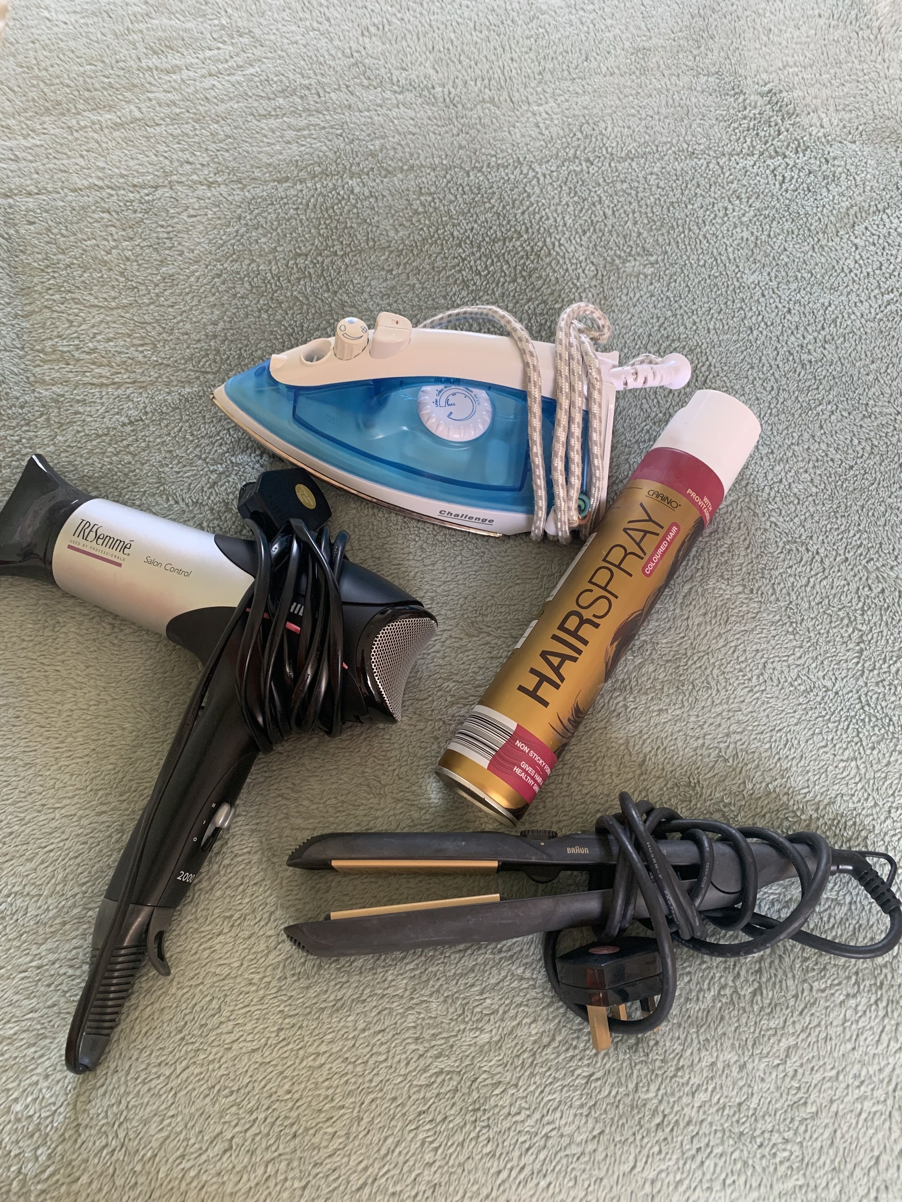 Variedad de productos para el cuidado del cabello, incluyendo una plancha, un aerosol fijador y una herramienta para peinar, sobre una superficie texturizada.