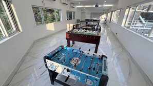A spacious indoor area with two foosball tables, large windows, and a projector screen. -  360 South, Khandala (Mawal)