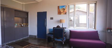 A modern living room with a purple sofa, a blue chair, a dining table, and a kitchen area with cabinets and a countertop.