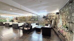A modern lounge area with seating arrangements, a stone wall with murals, and a motorcycle mounted on the wall. -  360 South, Khandala (Mawal)