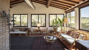 Un salón espacioso con techo alto, ventanas amplias, muebles de mimbre y una mesa de centro.
