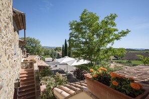 Edificio de piedra con tejas de arcilla, una escalera y vistas a un paisaje rural con árboles y campos.