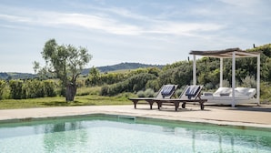 Una piscina con sillas de descanso y una pérgola, rodeada de vegetación y colinas.