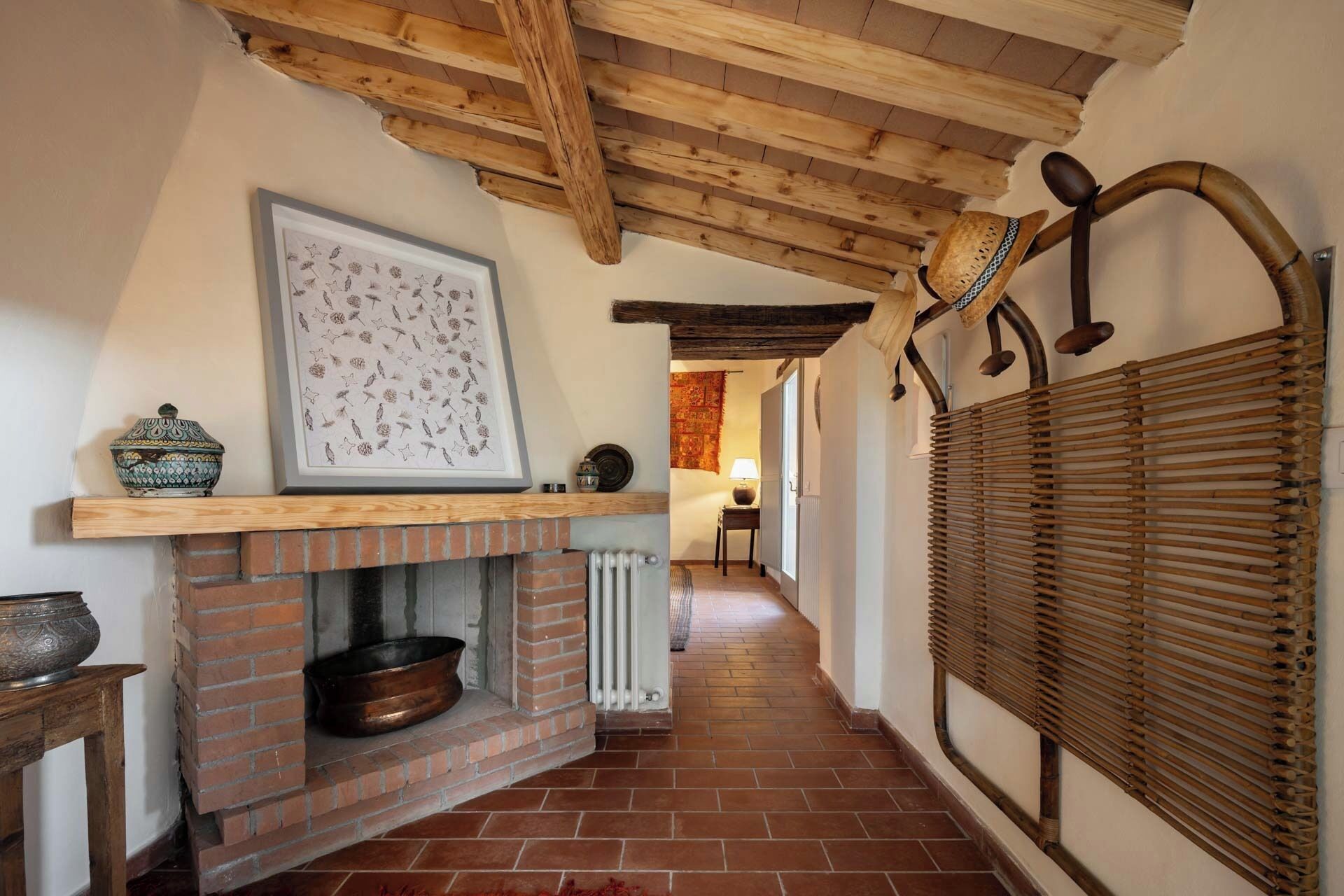 A hallway with a brick fireplace, a framed picture, and a traditional woven screen.