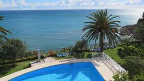 Ein Pool mit Blick aufs Meer, umgeben von Palmen und Liegestühlen.