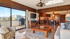 Un vaste espace de vie comprenant une grande porte-fenêtre coulissante donnant sur un balcon, une table basse en bois, un canapé et un coin cuisine avec un bar.