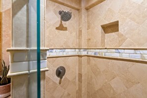 Une douche équipée d’un pommeau de douche à main, d’un panneau de commande mural et d’une étagère d’angle.