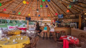 Un restaurant en plein air avec un toit de chaume, des tables rondes et des chaises.