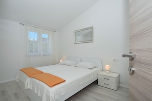 A bedroom with a bed, two bedside tables, a nightstand, a mirror, and a window with curtains.