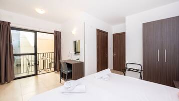 Una habitación de hotel con cama, escritorio, silla, armario y balcón con barandilla.