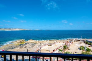 A coastal hotel with a view of the sea, featuring a parking area, outdoor seating, and a small garden.