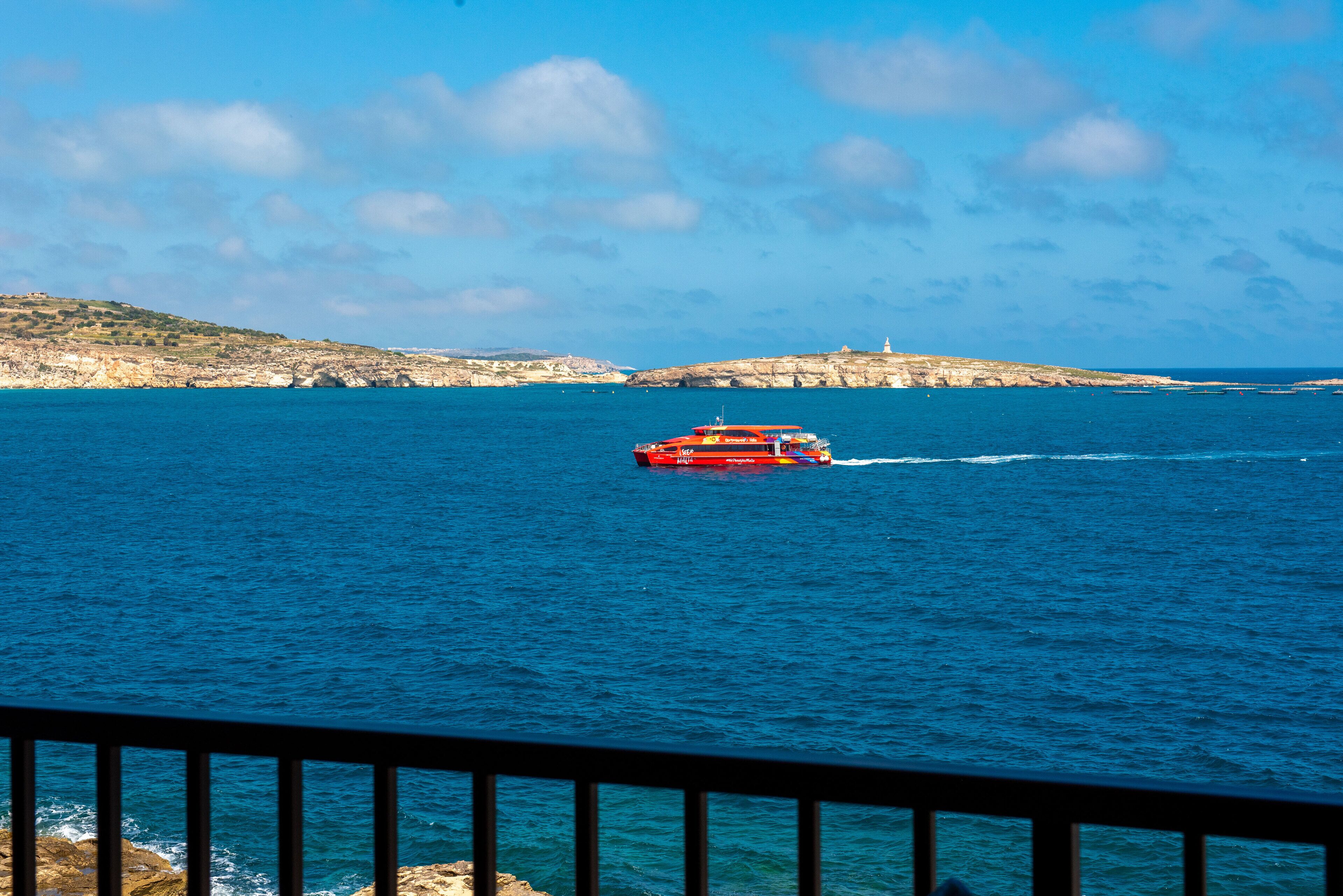 Un bateau rouge sur une mer calme, avec des falaises rocheuses en arrière-plan.