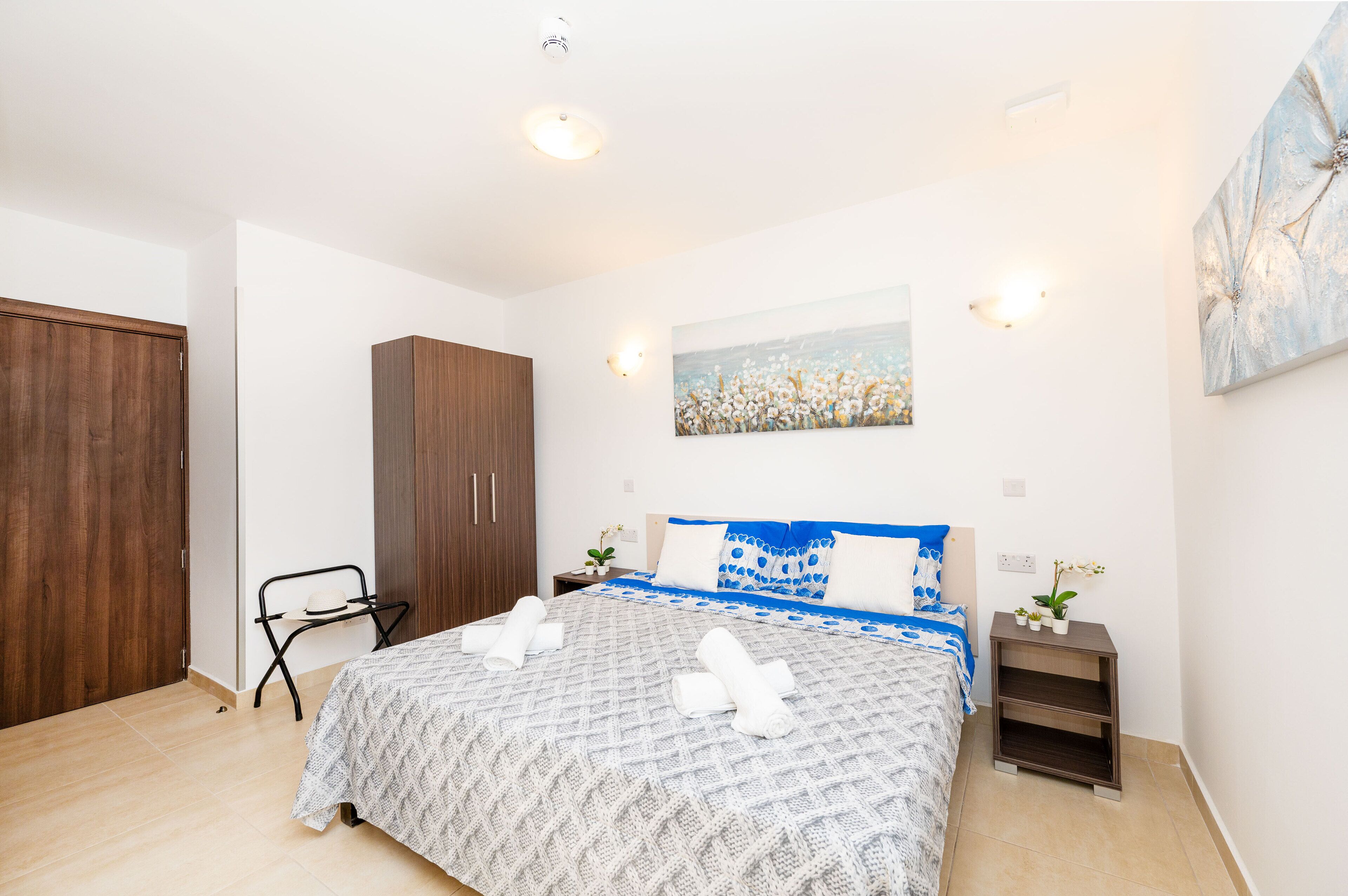 Quarto com uma cama, um guarda-roupa de madeira, uma mesa de cabeceira com uma planta e um quadro na parede.