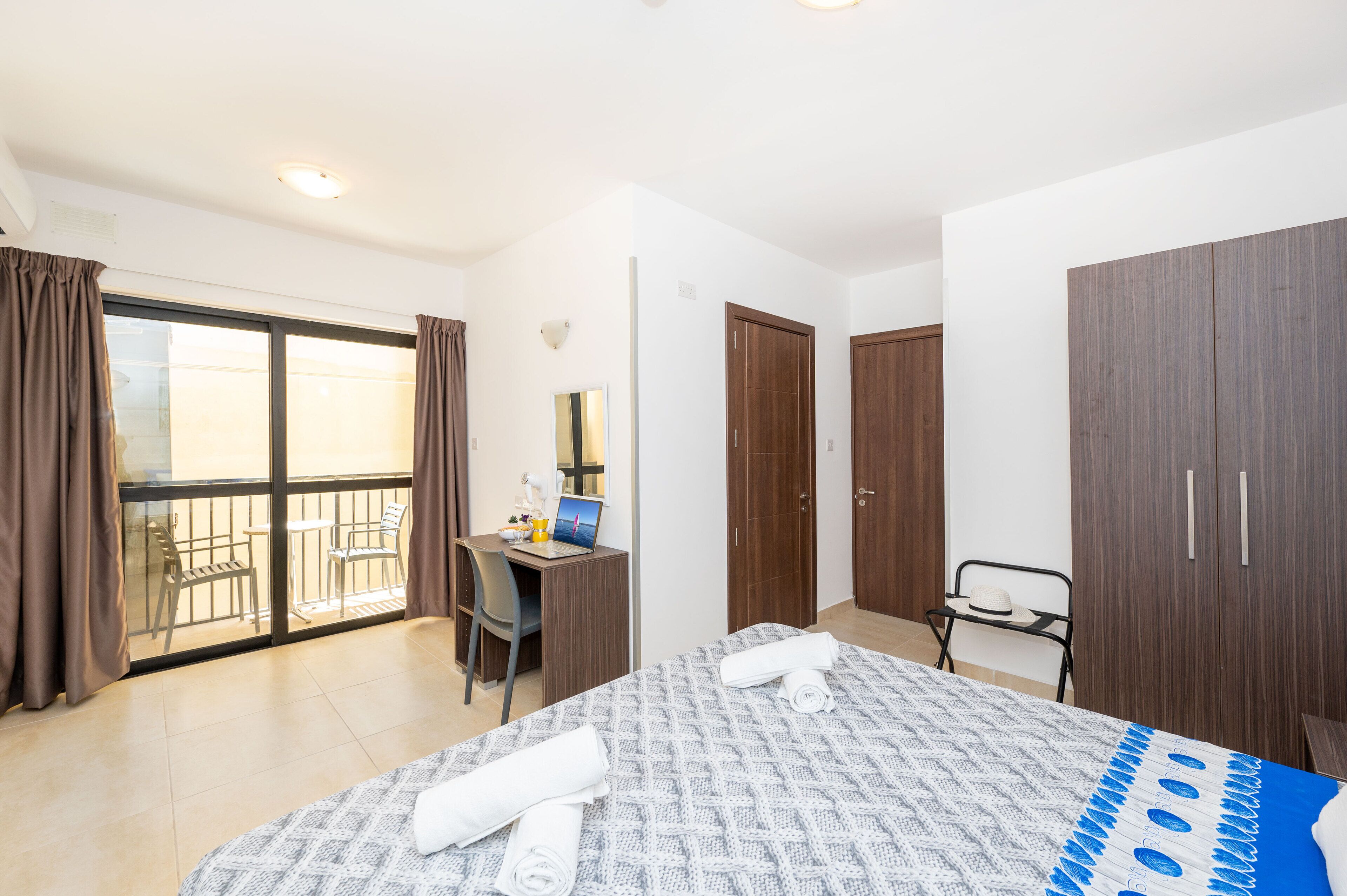 A hotel room with a bed, a desk, a computer, a chair, and a wardrobe.