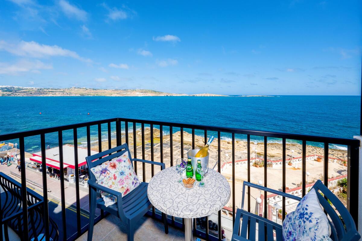 A balcony with a table, chairs, and a view of the sea and beach.