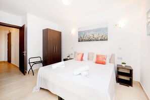 A hotel room with a large bed, a wooden wardrobe, a small bedside table, and a painting on the wall. - Islet Seafront Family Apartment  (St. Paul's Bay)