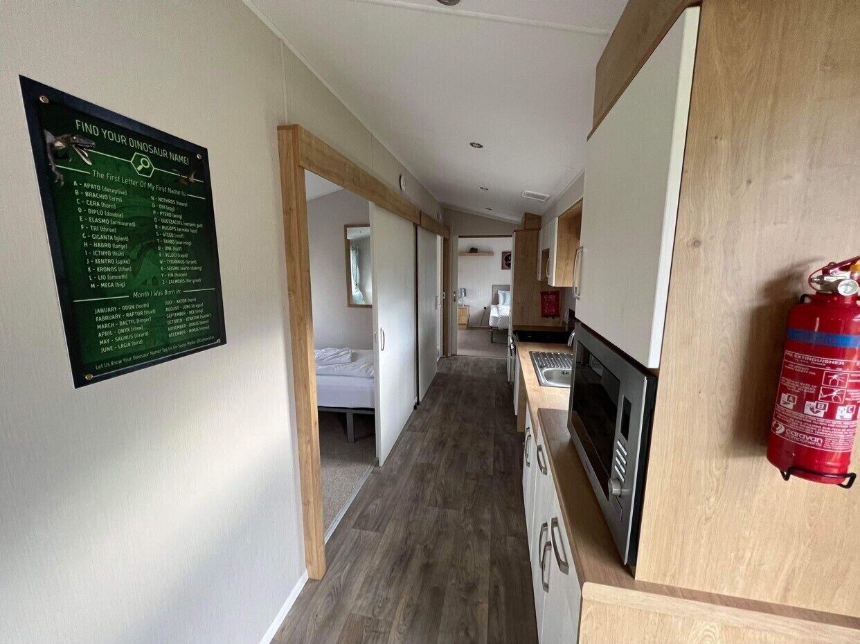 A narrow hallway with a wooden floor, a kitchen area with a microwave and sink, and a fire extinguisher mounted on the wall.