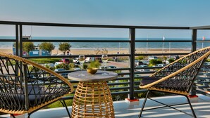 A balcony with wicker chairs and a small table, overlooking a beach and the sea. - Hôtel Spa Face à la Mer (Merville-Franceville-Plage)