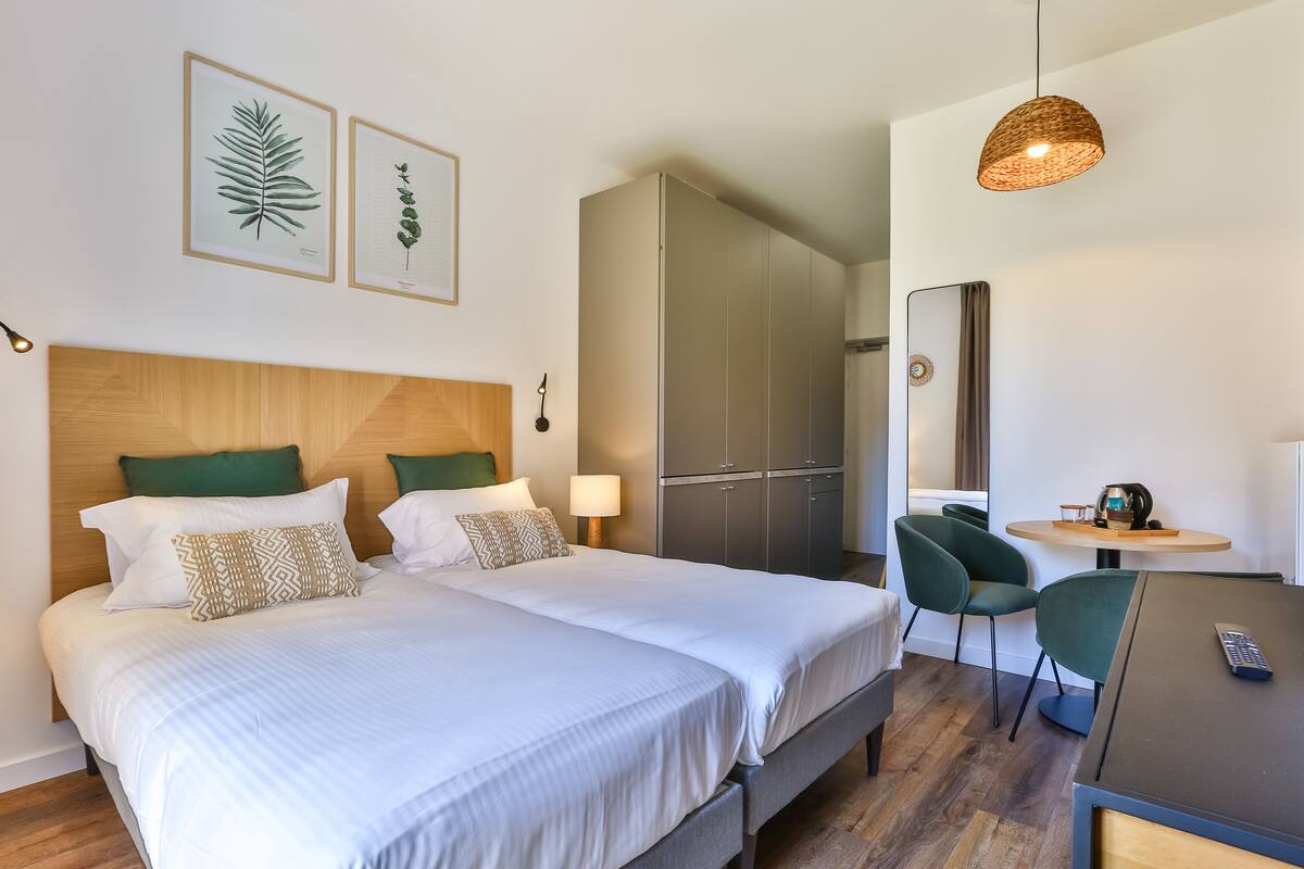 A hotel room with a double bed, a desk with a chair, a wardrobe, and framed botanical prints on the wall.