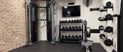 A gym with a brick wall, a television, and various exercise equipment including dumbbells and a bench press.