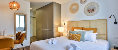 A modern hotel room with a large bed, a dining area with a table and chairs, and a view of the city through a window.