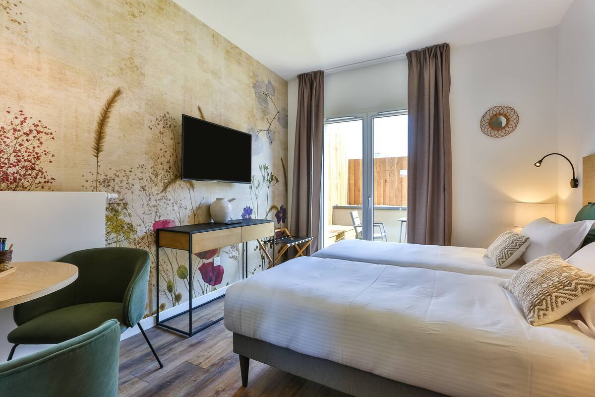 A hotel room with a bed, a desk, a chair, a TV, and a window with curtains.