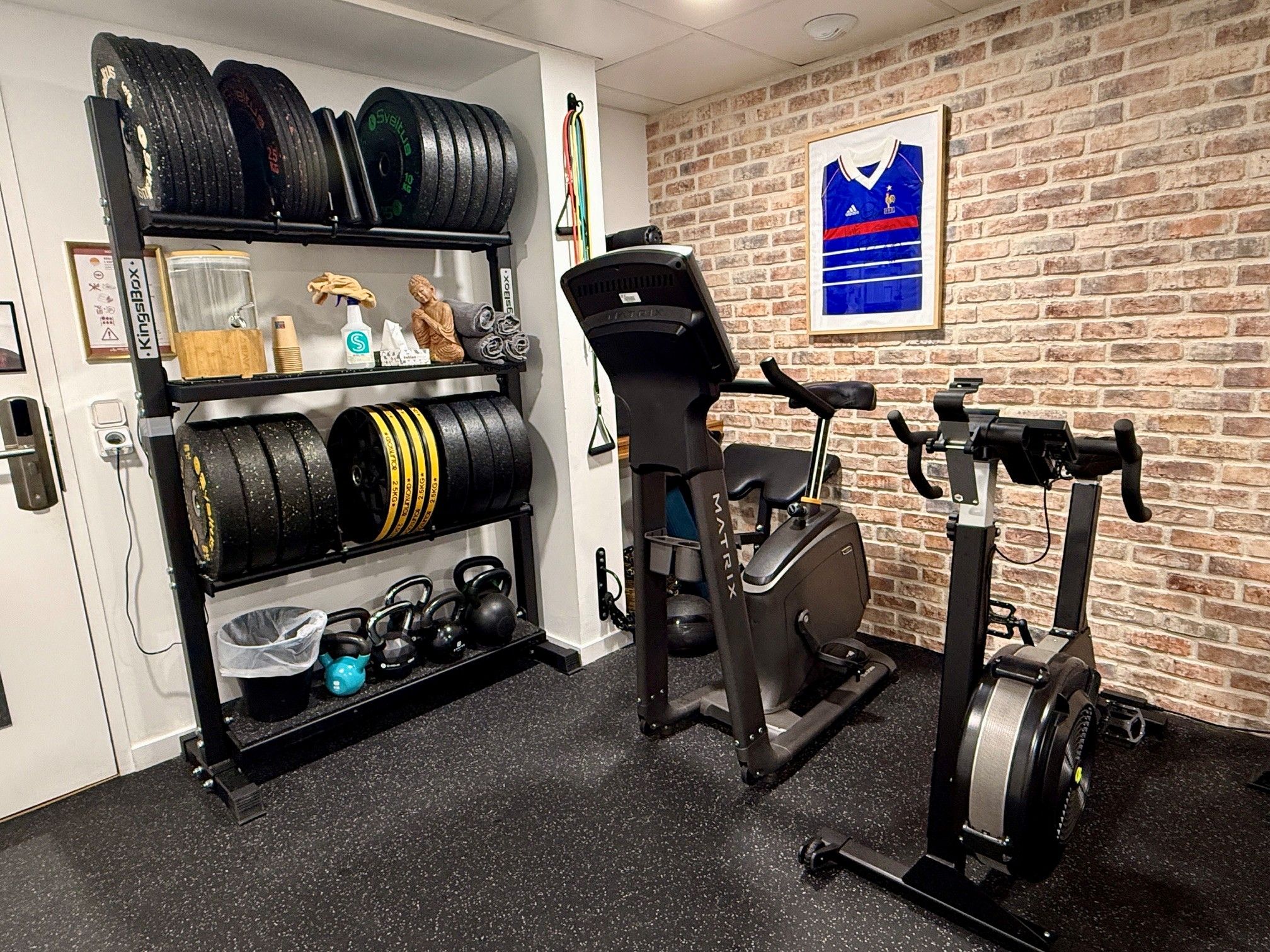 A home gym with a brick wall, a framed sports jersey, and exercise equipment including a treadmill and stationary bike.