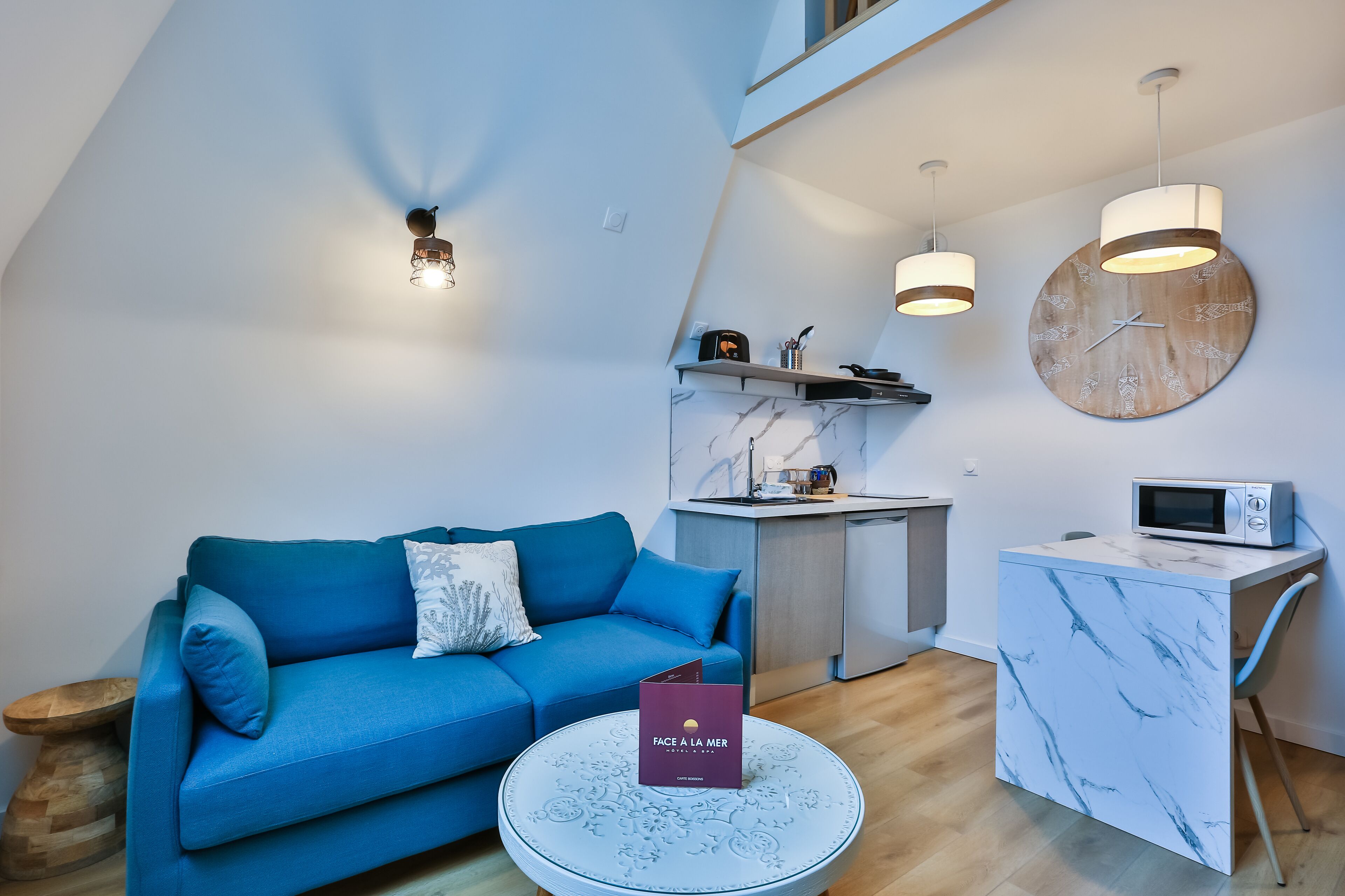 Un salon moderne avec un canapé bleu, une table basse en marbre et un coin cuisine équipé d’un four à micro-ondes.