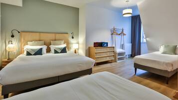 A hotel room with two beds, a wooden headboard, a bedside table with a lamp, a wardrobe, and a hanging coat rack.