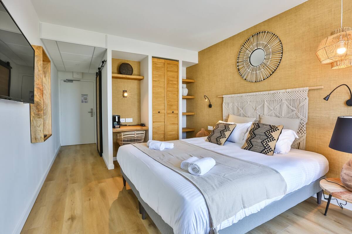 A modern bedroom with a large bed, wooden headboard, and a wall-mounted mirror.