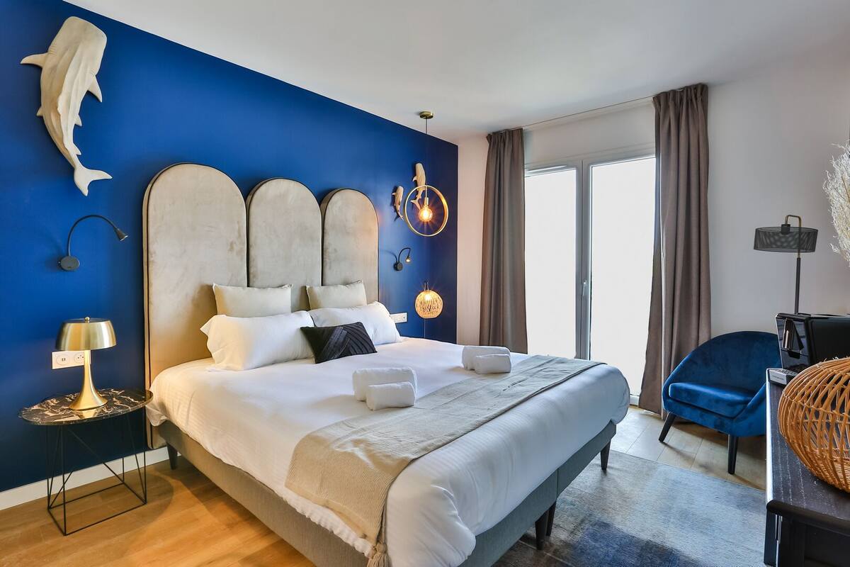 A modern bedroom with a large bed, a blue accent wall, and a large window.