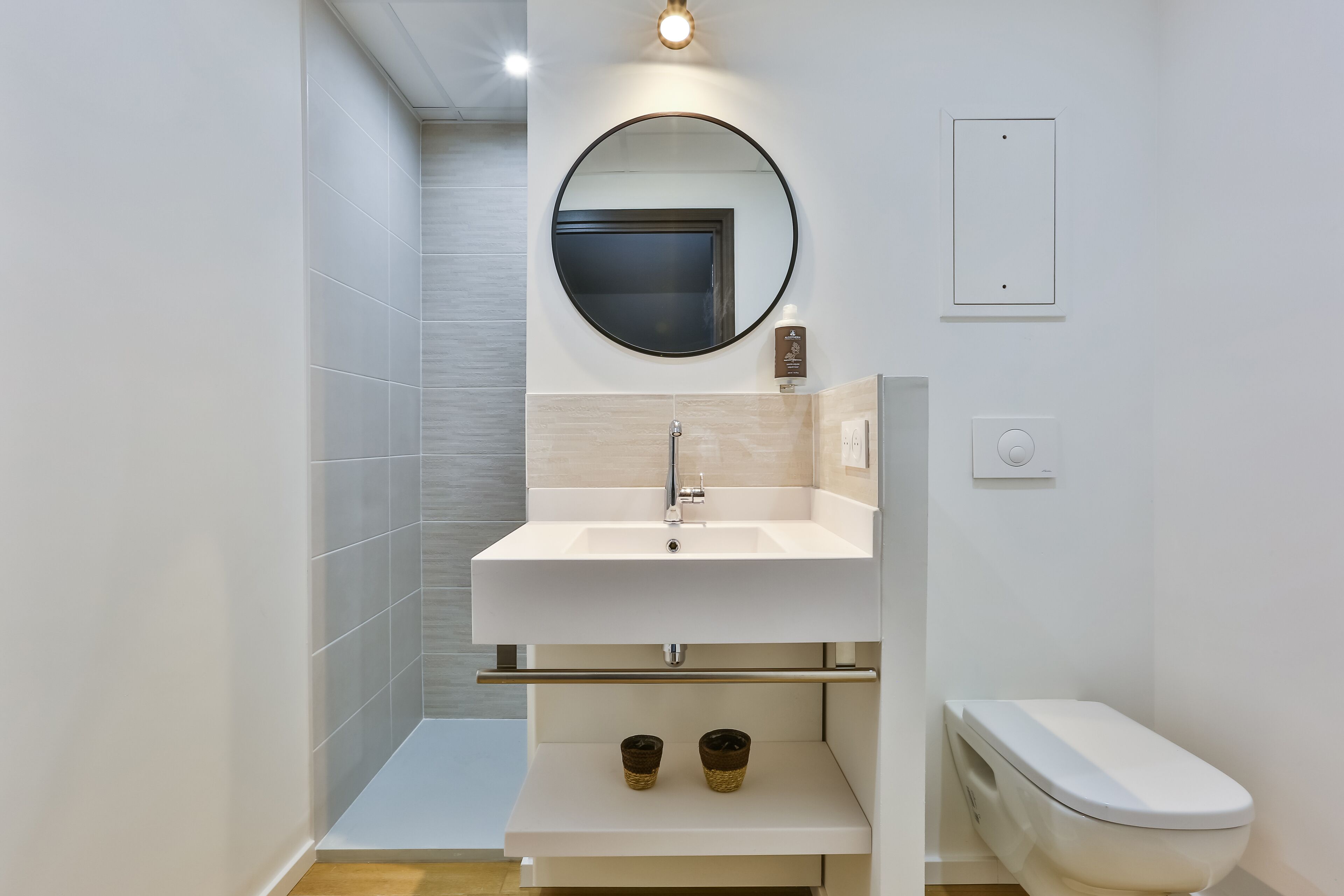 Un baño moderno con un lavabo blanco, un espejo redondo y un inodoro.
