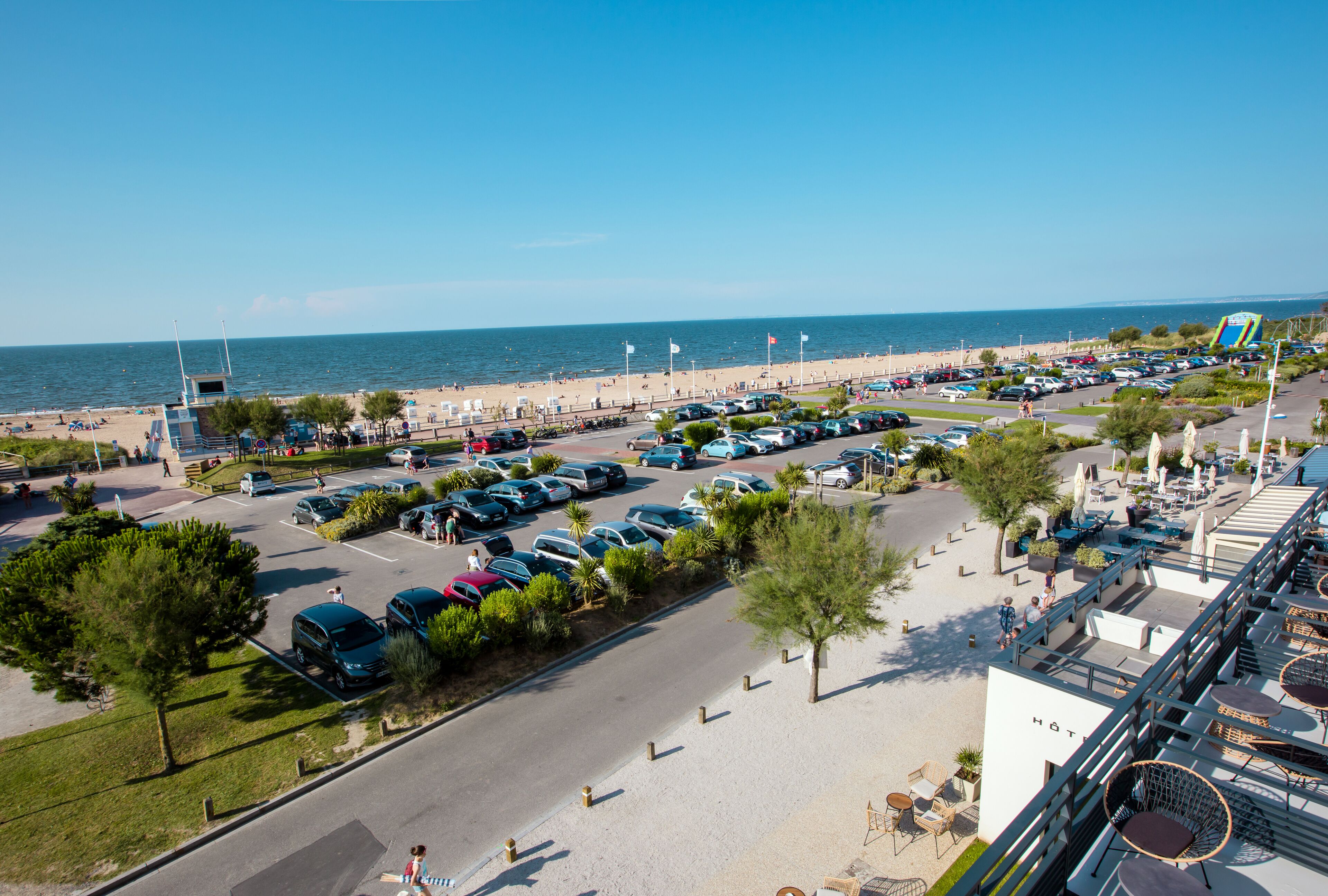 A hotel with outdoor seating overlooking a beach and parking area.