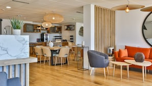 A modern interior with a dining area, a living space with a sofa and chairs, and a kitchen in the background. - Hôtel Spa Face à la Mer (Merville-Franceville-Plage)