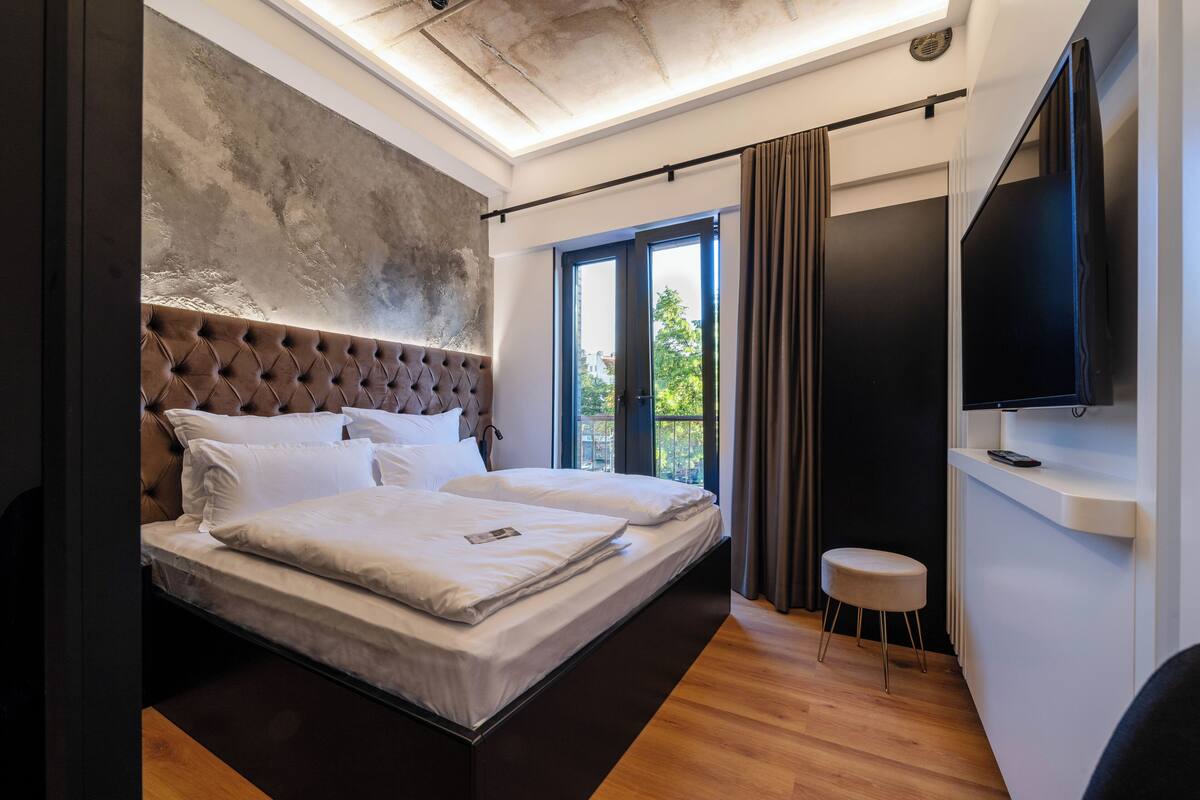A modern bedroom with a large bed, a television, and a view of the outdoors.