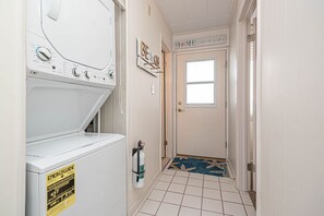 Ein Waschraum mit einer weißen Waschmaschine und einem Trockner, einem Feuerlöscher und einer Tür mit der Aufschrift 'HOME'.