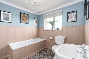 Ein Badezimmer mit Badewanne, Toilette und Waschbecken, mit einem Musterfliesenboden und Wandbildern.