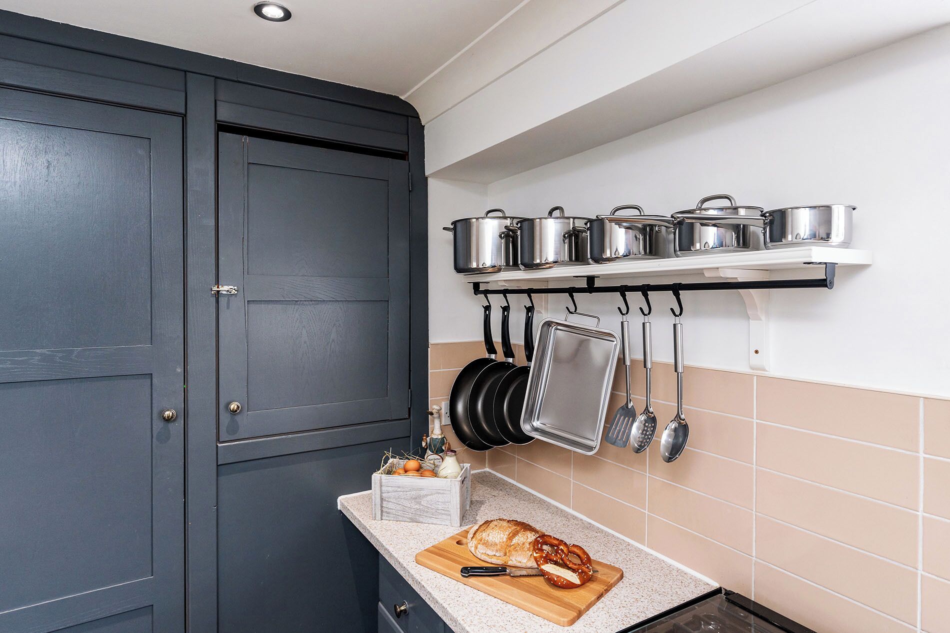 Een keuken met donkere kastjes, een aanrecht met een brood en een pretzel, en pannen op een wandrek.