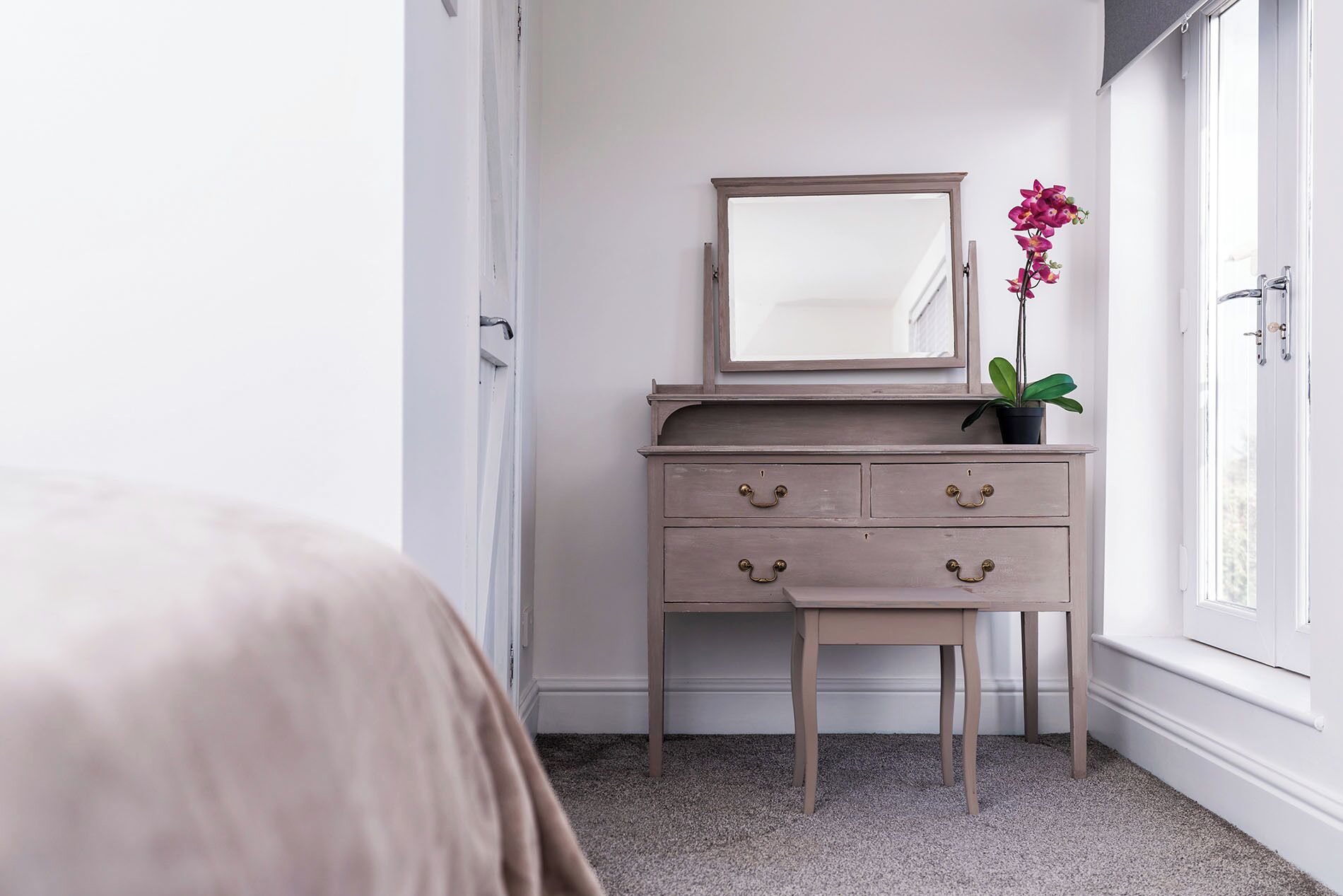 Un dormitorio con cama, cómoda con cajones, espejo, planta en maceta y ventana.