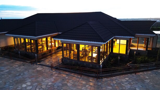 A building with a dark roof and large windows, stone flooring, and a staircase leading to the entrance.