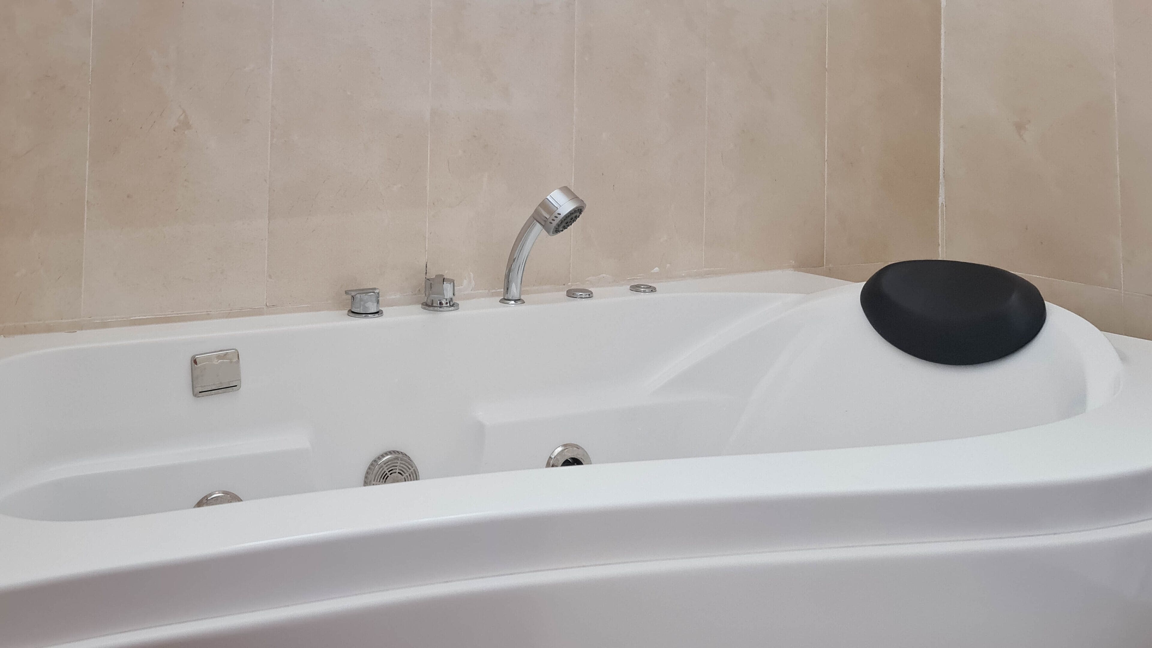 Una vasca da bagno bianca con un tappetino da bagno nero, un soffione a mano e un pannello di controllo.