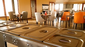 A kitchen area with stainless steel appliances, a dining area with multiple tables and chairs, and a view of the adjacent room.