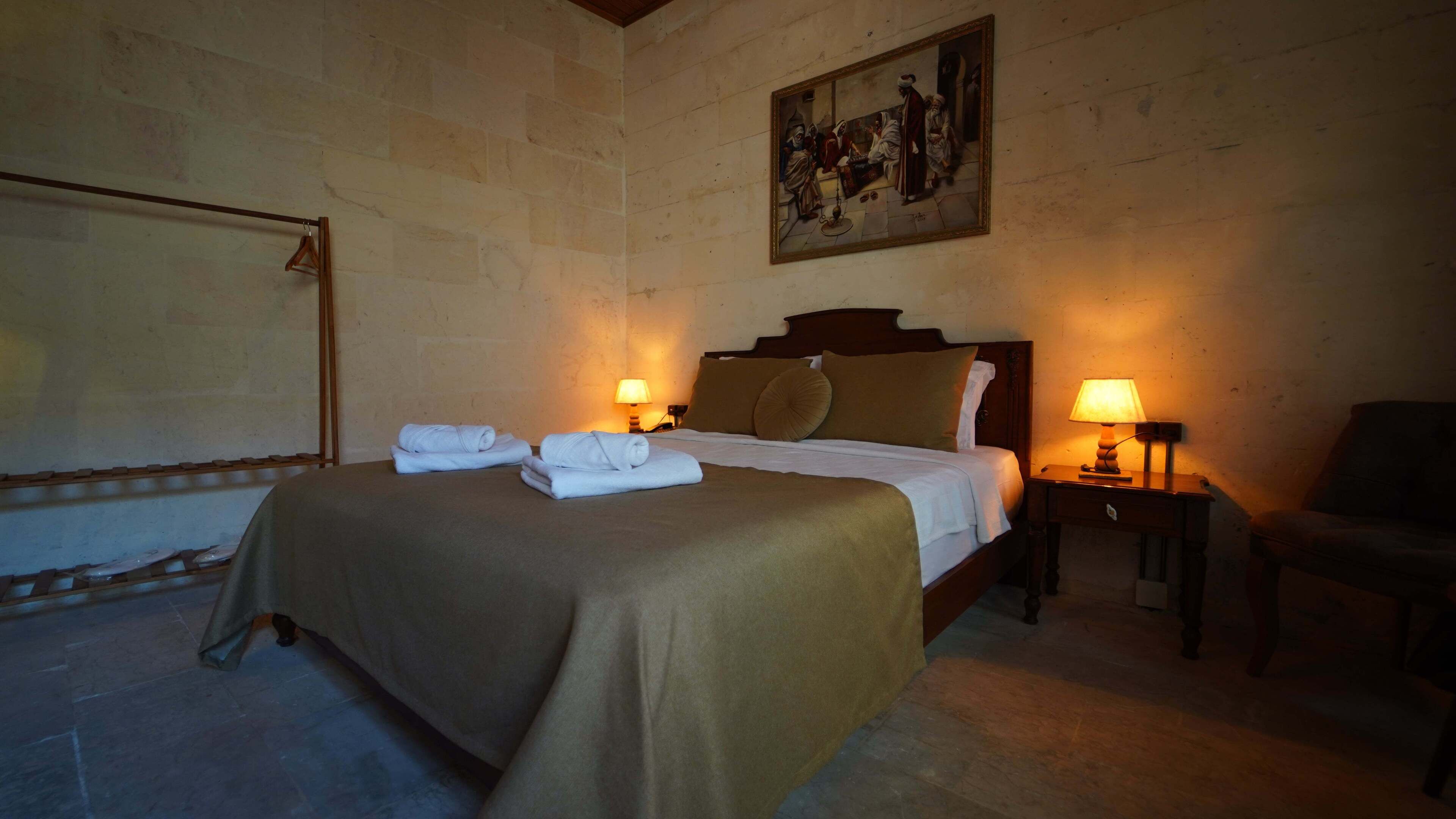 A hotel room with a large bed, two bedside lamps, a wooden headboard, and a painting on the wall.
