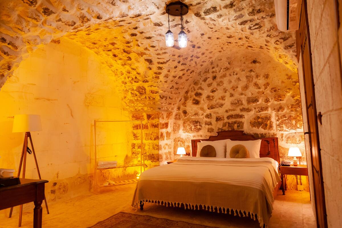 A cozy, stone-walled bedroom with a bed, two bedside lamps, and a wooden nightstand.