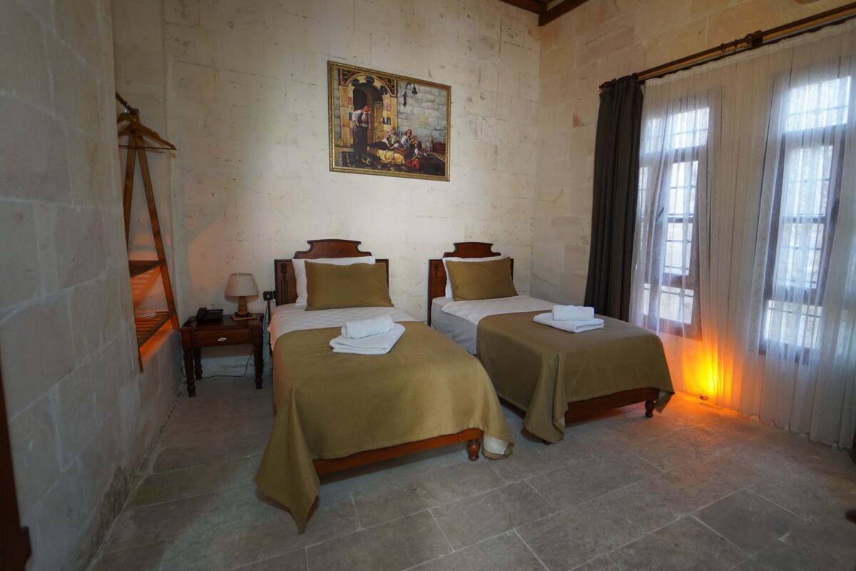 A hotel room with two beds, a painting on the wall, and a window with curtains.