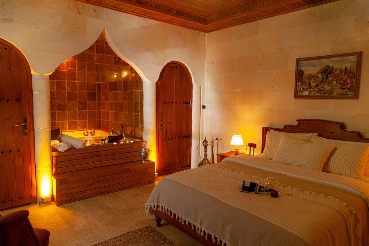 A bedroom with a large bed, wooden arched door, and a painting on the wall.