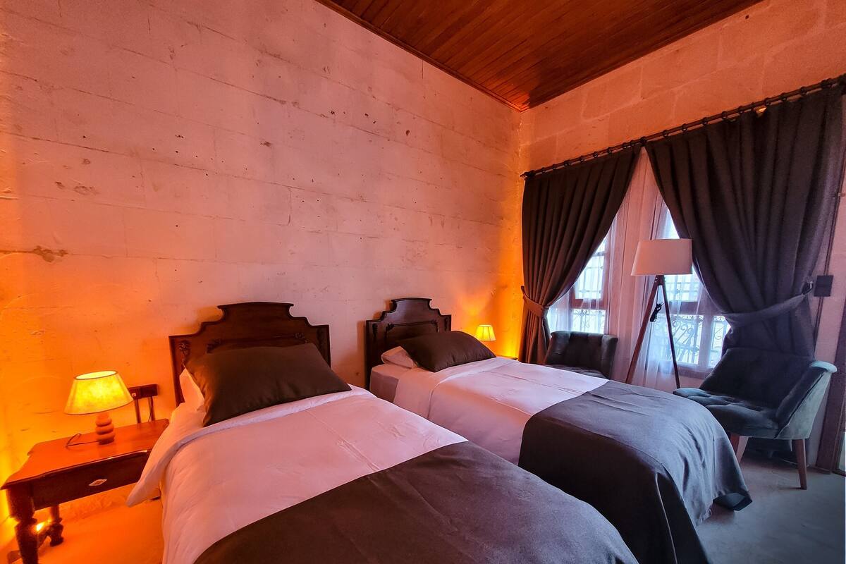 A room with two beds, a chair, a lamp, and a window with curtains.