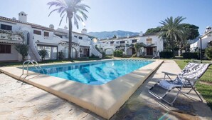A swimming pool with a palm tree and lounge chairs in a courtyard surrounded by buildings with balconies and a mountain in the background. - Apartment Sol de Denia. Wifi, A/C (Dénia)